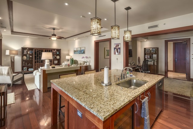 kitchen featuring light stone countertops, sink, hanging light fixtures, and a center island with sink