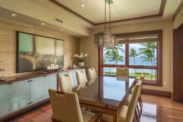 dining space with crown molding, hardwood / wood-style flooring, and a raised ceiling