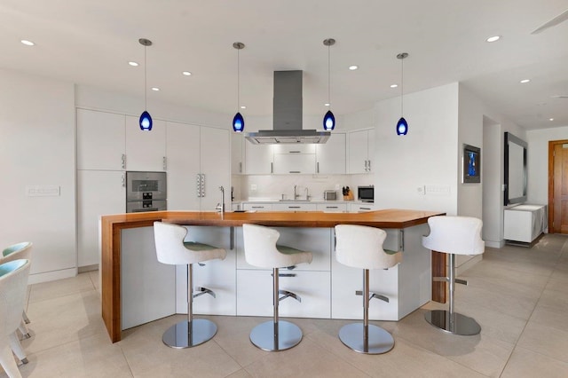 kitchen featuring white cabinetry, butcher block countertops, decorative light fixtures, a kitchen bar, and island range hood