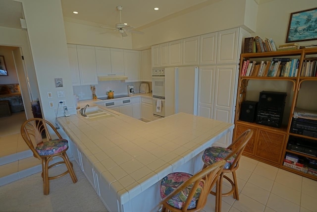 kitchen with a kitchen bar, black electric cooktop, ceiling fan, white cabinetry, and tile countertops