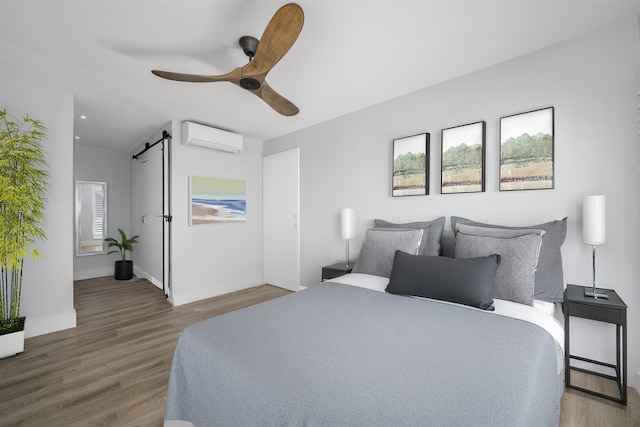 bedroom featuring a barn door, ceiling fan, wood-type flooring, and a wall mounted air conditioner