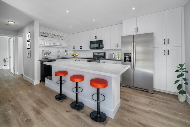 kitchen featuring black appliances, white cabinets, a center island, light hardwood / wood-style floors, and a breakfast bar area