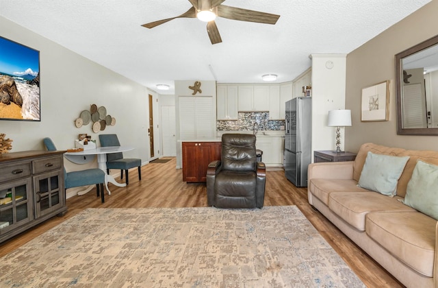 living room featuring ceiling fan, sink, a textured ceiling, and light wood-type flooring