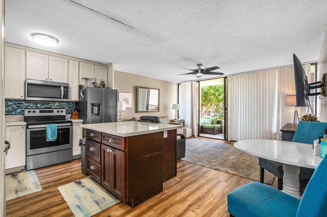 kitchen with light wood-type flooring, stainless steel appliances, a textured ceiling, and backsplash