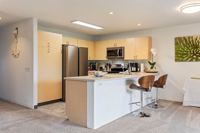 kitchen with light brown cabinets, kitchen peninsula, light colored carpet, and stainless steel appliances