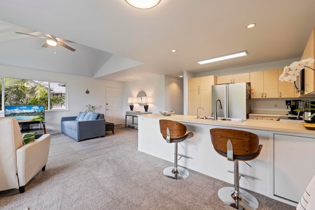 kitchen with ceiling fan, a breakfast bar area, fridge, light colored carpet, and vaulted ceiling