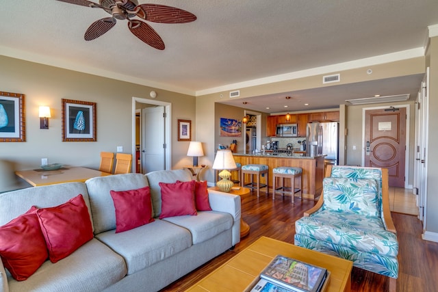 living room featuring dark wood-type flooring, ceiling fan, crown molding, and a textured ceiling