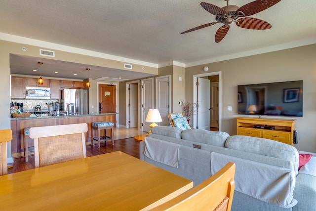 living room with dark wood-type flooring, crown molding, a textured ceiling, and ceiling fan