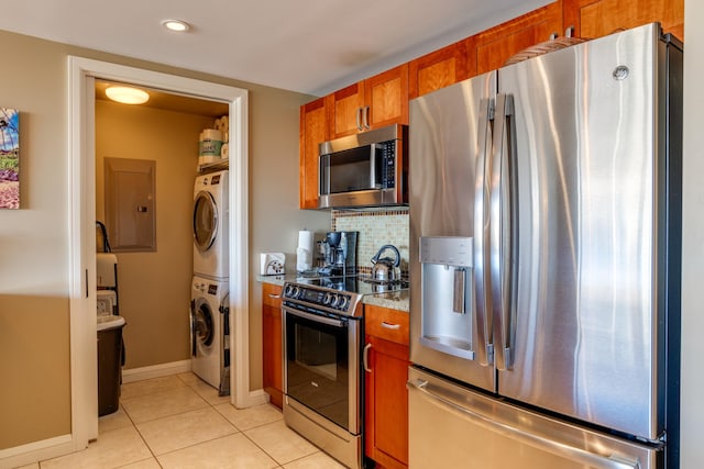 kitchen with electric panel, stacked washer / dryer, light tile patterned floors, light stone countertops, and stainless steel appliances