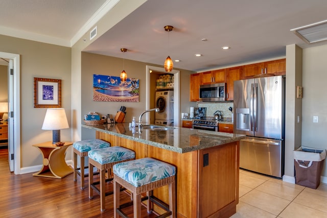 kitchen featuring washer / clothes dryer, stainless steel appliances, dark stone counters, sink, and decorative light fixtures