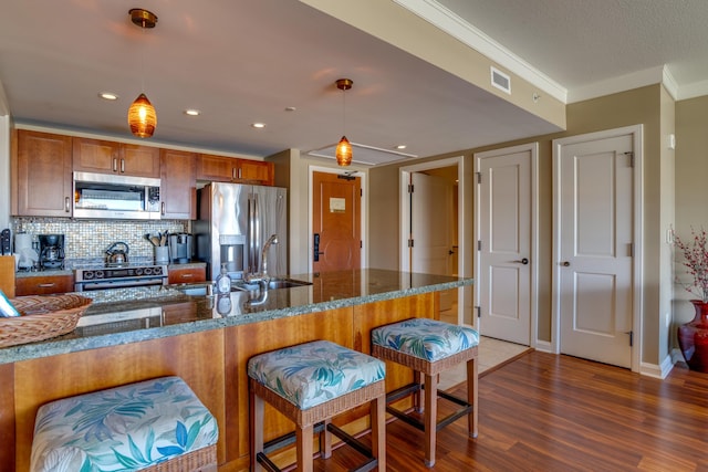 kitchen with dark stone counters, crown molding, decorative light fixtures, appliances with stainless steel finishes, and dark hardwood / wood-style flooring