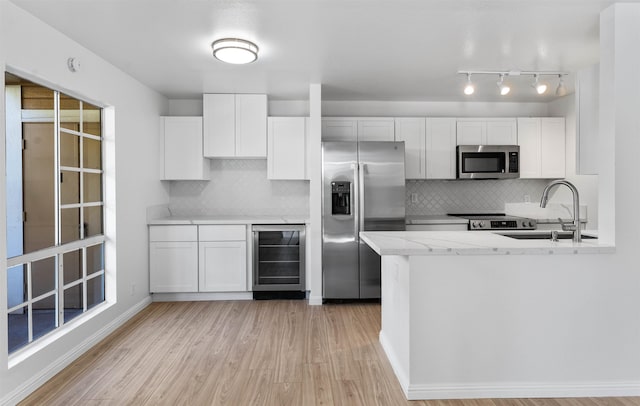 kitchen featuring appliances with stainless steel finishes, beverage cooler, white cabinets, and a sink