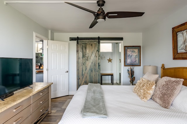 bedroom with ceiling fan, dark wood-type flooring, and a barn door