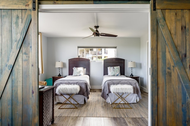 bedroom featuring ceiling fan, a barn door, and hardwood / wood-style floors