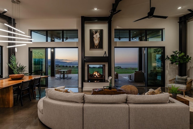 living room with a towering ceiling, concrete floors, ceiling fan, and a multi sided fireplace