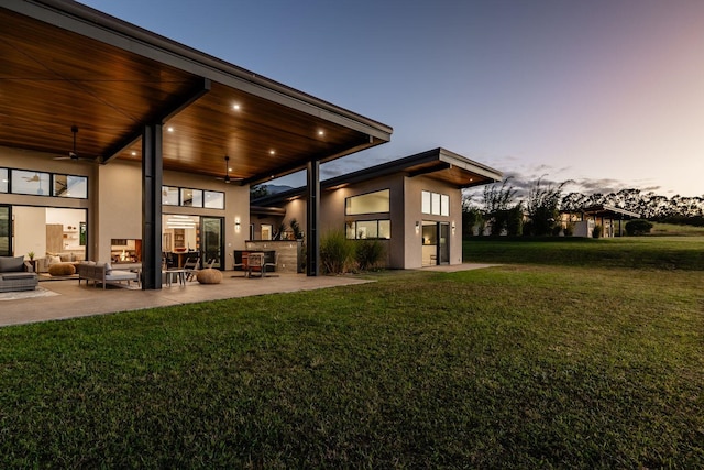 back house at dusk with ceiling fan, a patio area, and a lawn