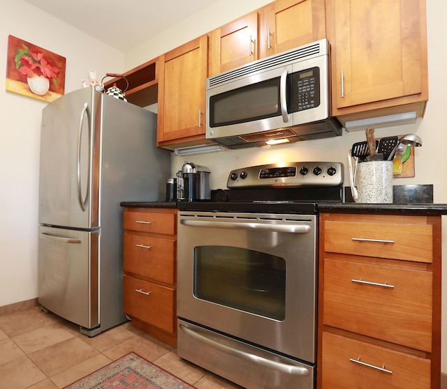 kitchen with stainless steel appliances, dark stone counters, and light tile patterned flooring