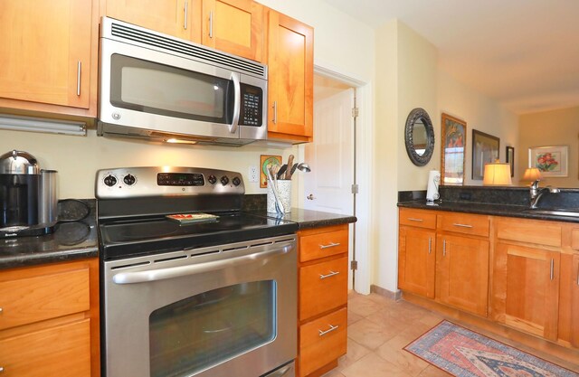 kitchen with appliances with stainless steel finishes, light tile patterned flooring, sink, and dark stone counters