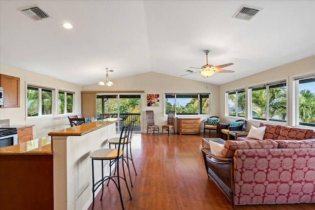 living room with ceiling fan with notable chandelier, dark hardwood / wood-style flooring, and vaulted ceiling