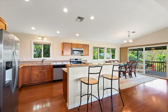 kitchen featuring sink, a center island, pendant lighting, stainless steel appliances, and light stone countertops