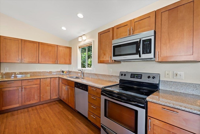 kitchen featuring vaulted ceiling, appliances with stainless steel finishes, sink, light stone counters, and light hardwood / wood-style floors