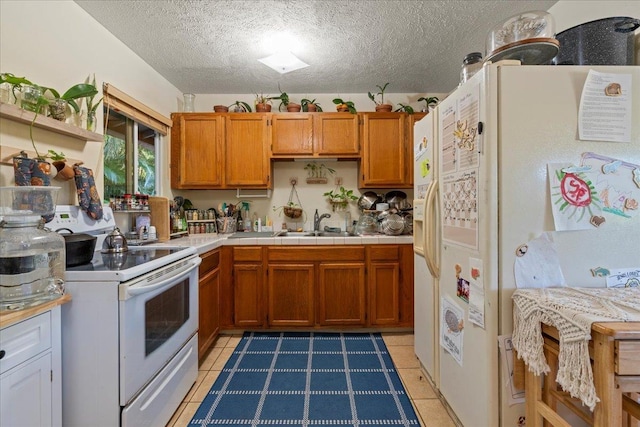 kitchen featuring sink, white appliances, a textured ceiling, dark tile patterned flooring, and tile countertops