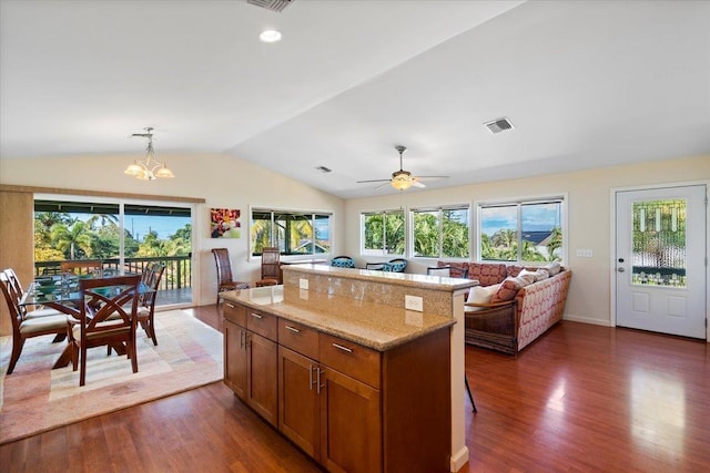 kitchen with lofted ceiling, hanging light fixtures, dark hardwood / wood-style floors, a center island, and light stone countertops