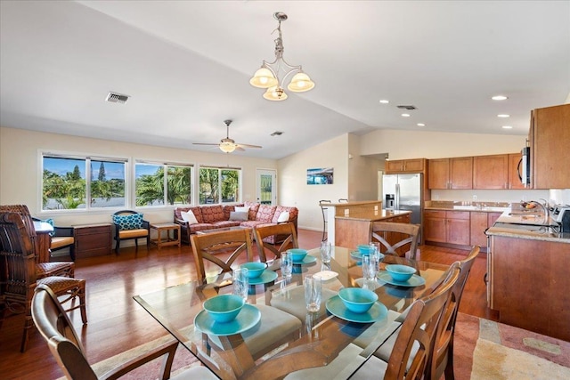 dining area with ceiling fan with notable chandelier, wood-type flooring, and vaulted ceiling