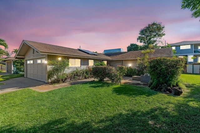 single story home featuring a garage, a lawn, driveway, and solar panels