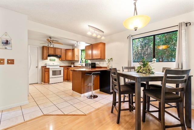 kitchen featuring a peninsula, under cabinet range hood, brown cabinetry, and electric stove