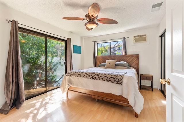 bedroom with a textured ceiling, a wall mounted air conditioner, visible vents, and light wood-style floors