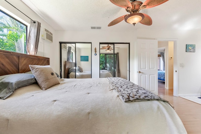 bedroom featuring visible vents, a ceiling fan, wood finished floors, a textured ceiling, and multiple closets