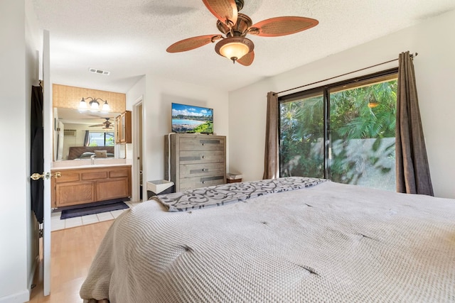 bedroom with visible vents, a ceiling fan, ensuite bathroom, a textured ceiling, and light wood-type flooring