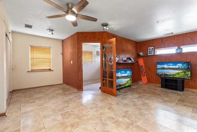 living room featuring a ceiling fan, visible vents, and wood walls