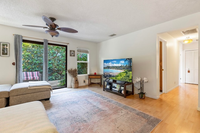 living room featuring visible vents, a ceiling fan, a textured ceiling, wood finished floors, and baseboards