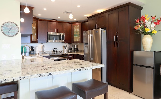 kitchen featuring a kitchen breakfast bar, sink, appliances with stainless steel finishes, light stone counters, and kitchen peninsula