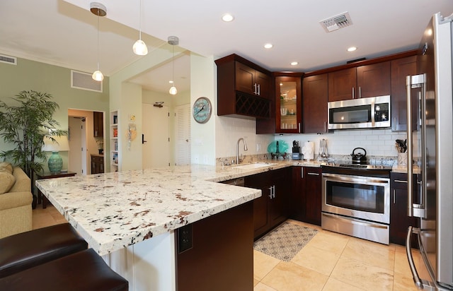 kitchen featuring kitchen peninsula, a kitchen bar, stainless steel appliances, sink, and decorative light fixtures