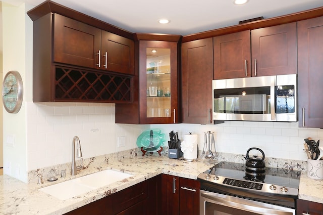 kitchen with backsplash, light stone counters, sink, and stainless steel appliances