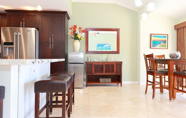 kitchen featuring lofted ceiling, stainless steel fridge, high quality fridge, decorative light fixtures, and light stone counters