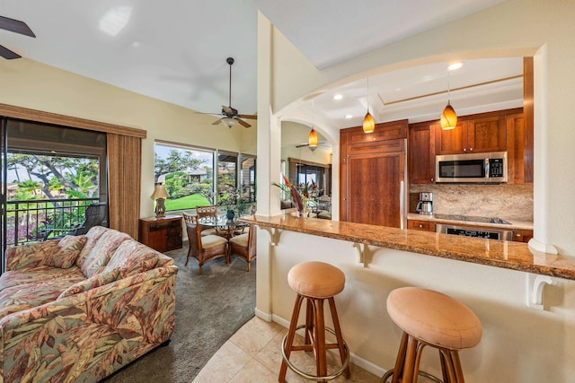 kitchen featuring backsplash, hanging light fixtures, paneled refrigerator, light tile patterned floors, and a breakfast bar area