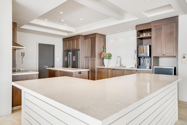 kitchen featuring stainless steel fridge, black electric cooktop, a spacious island, wall chimney range hood, and light tile patterned flooring