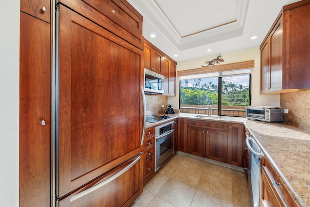 kitchen with tasteful backsplash, ornamental molding, stainless steel appliances, a tray ceiling, and sink