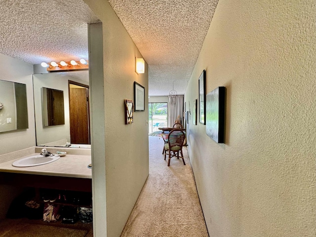 hall with sink, light colored carpet, and a textured ceiling