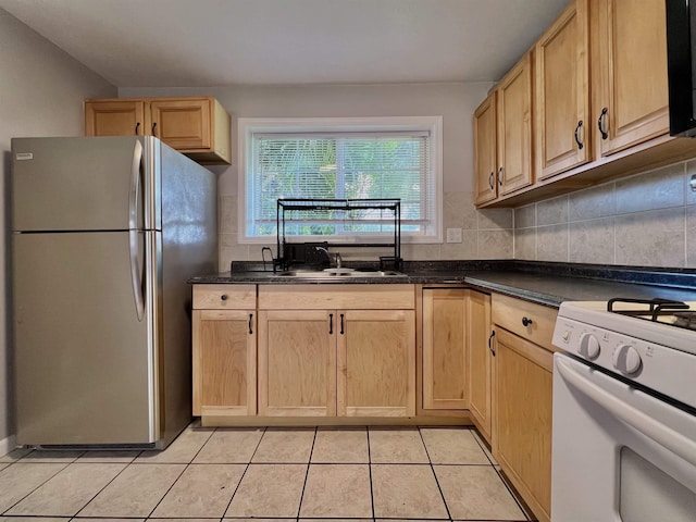 kitchen featuring light brown cabinetry, sink, white range with gas stovetop, light tile patterned floors, and stainless steel refrigerator