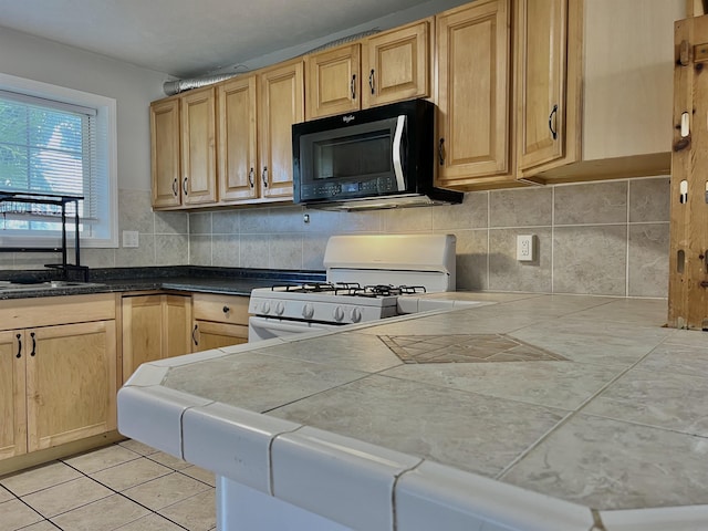 kitchen with white gas range, tile counters, and light brown cabinets