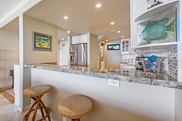 kitchen with tasteful backsplash, light stone countertops, stainless steel fridge, and white cabinets