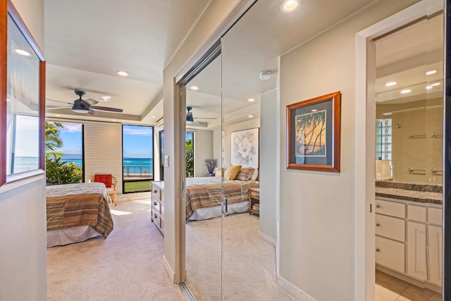 carpeted bedroom with connected bathroom, a water view, ceiling fan, and a closet