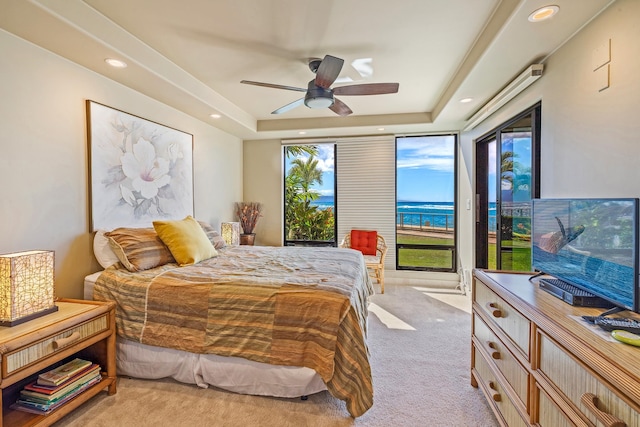 bedroom with multiple windows, light carpet, ceiling fan, and a raised ceiling