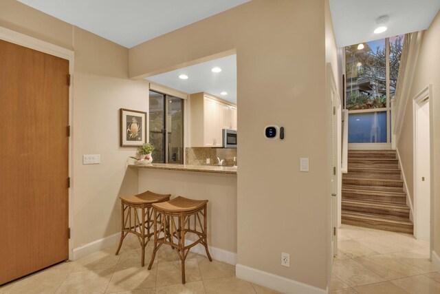 kitchen featuring a breakfast bar area, stainless steel microwave, backsplash, white cabinets, and baseboards