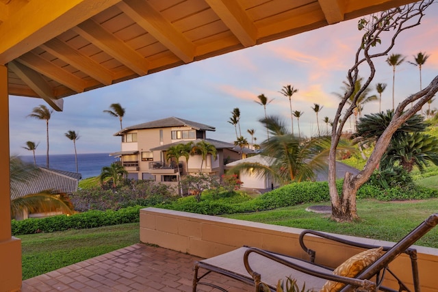 patio terrace at dusk featuring a lawn and a water view